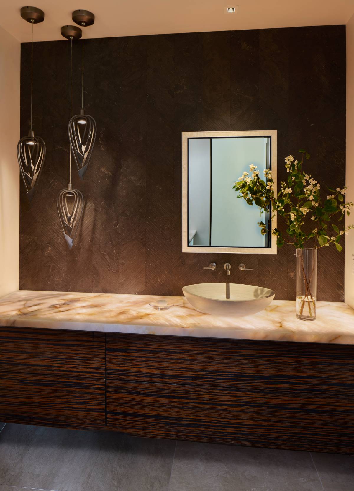 A moody powder room with a dark accent wall, statement lighting, and behind-the-sink lighting