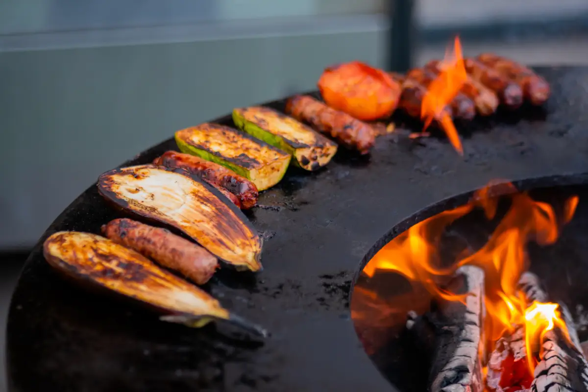 Process of cooking sausages, zucchini, eggplant, tomato on grill brazier at outdoor patio
