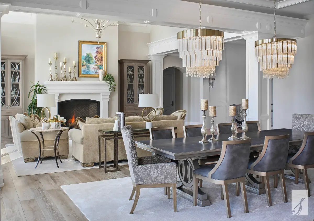 Open-concept living and dining room with twin crystal chandeliers over a pedestal dining table and facing sofas by the fireplace